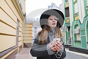 Portrait of a stylish woman listening to music in headphones on the background of the old town.