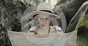 Stylish traveler girl in hat looking at map, exploring woods