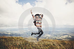 Stylish traveler hipster girl in hat, jumping with backpack and