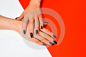 Stylish trendy female black manicure. Beautiful old woman`s hands on white and red background