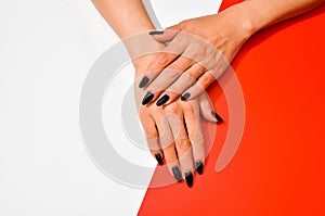 Stylish trendy female black manicure. Beautiful old woman`s hands on white and red background