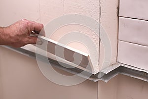 Stylish trendy white ceramic tiles on the kitchen wall. Hands in the process of laying white rectangular tiles on the