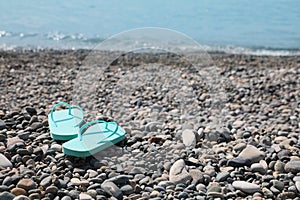 Stylish turquoise flip lops on pebble beach near sea. Space for text