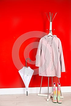Stylish umbrella, raincoat and boots near red wall