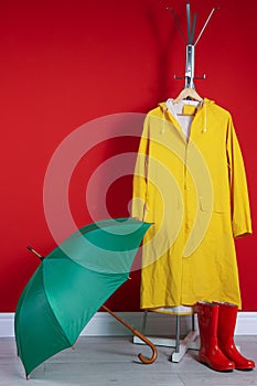 Stylish umbrella, raincoat and boots near wall