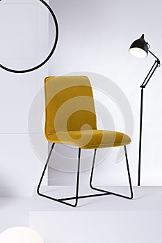 Stylish velvet yellow chair next to tall industrial black lamp in white interior