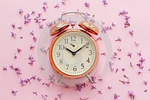 Stylish vintage alarm clock on pink background with lilac flower