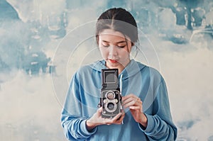 Stylish vintage female photographer  holding her old  twin lens camera to her chest as she composes her image with a serious photo