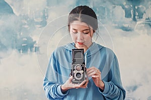 Stylish vintage female photographer  holding her old  twin lens camera to her chest as she composes her image with a serious