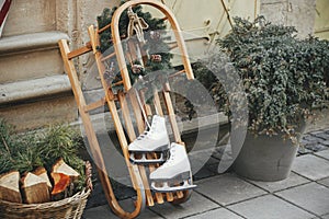 Stylish vintage ice skates and rustic wreath on wooden sleigh at building exterior. Modern christmas decor in city street. Winter
