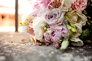 Stylish wedding bouquet flowers from bush roses, eustoma and gold wedding rings on the stone on the background nature. Wedding cer