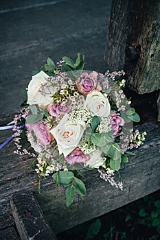 Stylish wedding bouquet of pink and white roses lies on a wooden bench