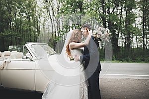 Stylish wedding couple, bride, groom kissing and hugging on retro car