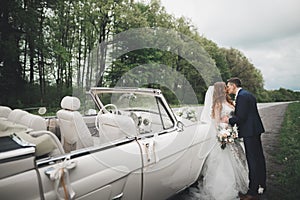 Stylish wedding couple, bride, groom kissing and hugging on retro car