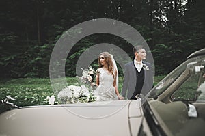 Stylish wedding couple, bride, groom kissing and hugging on retro car