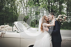 Stylish wedding couple, bride, groom kissing and hugging on retro car