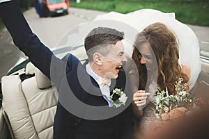 Stylish wedding couple, bride, groom kissing and hugging on retro car