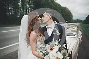 Stylish wedding couple, bride, groom kissing and hugging on retro car