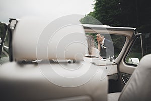 Stylish wedding couple, bride, groom kissing and hugging on retro car