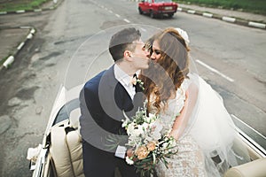 Stylish wedding couple, bride, groom kissing and hugging on retro car