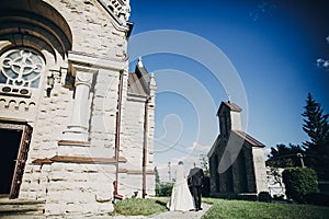 Stylish wedding couple walking at church after holy matrimony. Gorgeous bride and groom near church after wedding ceremony photo