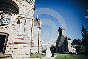 Stylish wedding couple walking at church after holy matrimony. Gorgeous bride and groom near church after wedding ceremony