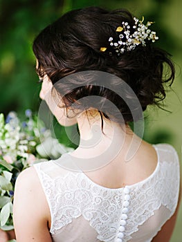 Stylish wedding hairdo. Bridal portrait in white lace wedding dress and oversized bouquet, rear view.