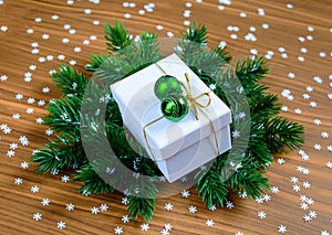Stylish white Christmas gift box with green baubles on fir tree branches and wooden background