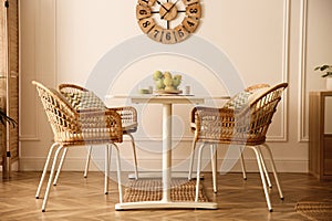 Stylish white dining table and wicker chairs in room. Interior