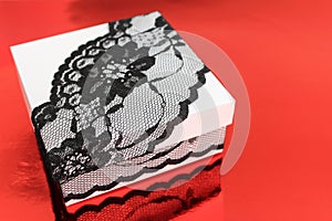 Stylish white gift box, decorated with black lace ribbon on red background