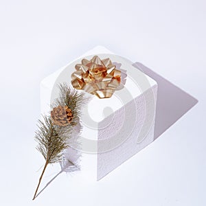 Stylish winter geometric scene white cube, gold bow and spruce branch  Minimal still life concept art. Winter, holiday, christmas