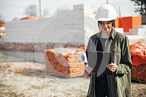 Stylish woman architect checking blueprints at construction site. Young female engineer or construction worker in hardhat looking