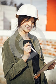 Stylish woman architect with tablet checking blueprints at construction site. Young female engineer or construction worker in