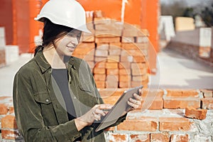 Stylish woman architect with tablet checking blueprints at construction site. Young female engineer or construction worker in