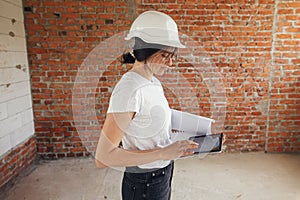 Stylish woman architect with tablet checking blueprints at construction site. Young female engineer or construction worker in