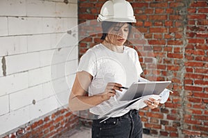 Stylish woman architect with tablet checking blueprints at construction site. Young female engineer or construction worker in