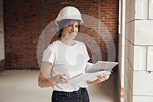 Stylish woman architect with tablet checking blueprints at construction site. Young female engineer or construction worker in