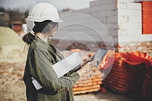 Stylish woman architect with tablet checking blueprints at construction site. Young female engineer or construction worker in