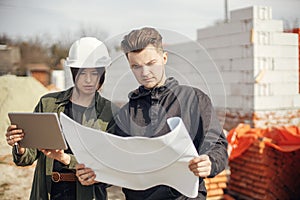 Stylish woman architect with tablet  and foreman checking blueprints at construction site. Young engineer and construction workers