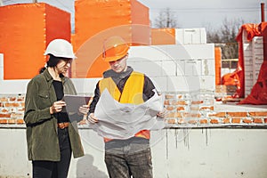 Stylish woman architect with tablet  and foreman checking blueprints at construction site. Young engineer and construction workers