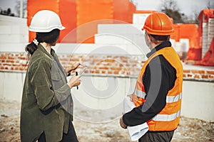 Stylish woman architect with tablet and senior foreman checking blueprints at construction site. Engineer and construction worker