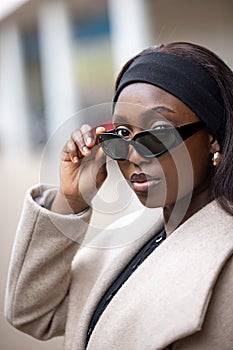 Stylish Woman in Beige Coat Adjusting Sunglasses on City Street