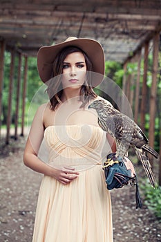 Stylish woman with bird outdoors. Perfect girl in fashionable dress and fedora hat