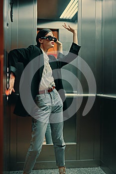 Stylish woman in black jacket and sunglasses posing in elevator, fashion model