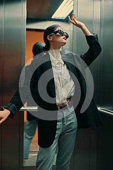 Stylish woman in black jacket and sunglasses posing in elevator, fashion model