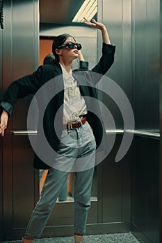 Stylish woman in black jacket and sunglasses posing in elevator, fashion model