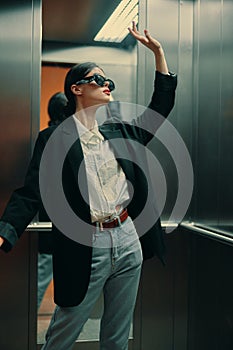 Stylish woman in black jacket and sunglasses posing in elevator, fashion model