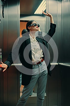 Stylish woman in black jacket and sunglasses posing in elevator, fashion model