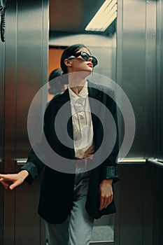 Stylish woman in black jacket and sunglasses posing in elevator, fashion model
