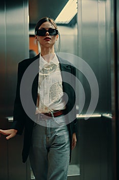 Stylish woman in black jacket and sunglasses posing in elevator, fashion model, dark cinematic light and color